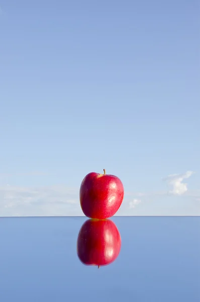 Een rode appel op spiegel en hemel — Stockfoto
