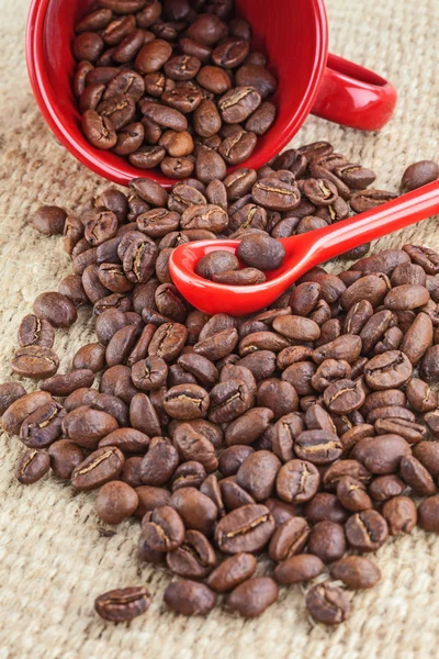 Spilled coffee seeds and red cup and spoon — Stock Photo, Image