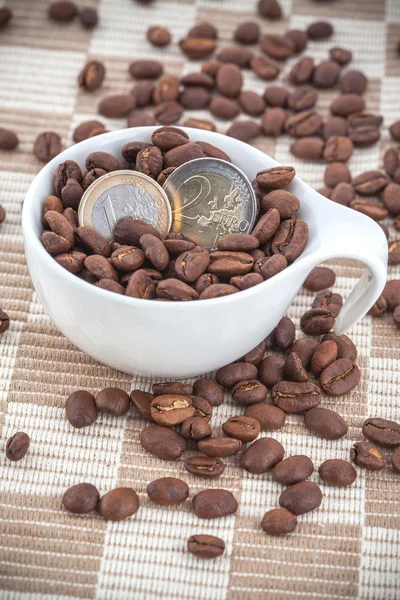 Filiżanka ceramiczna z nasionami kawy i monetami euro — Zdjęcie stockowe
