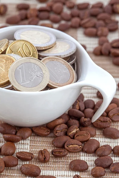 Filiżanka pełna monet euro, rozlane ziarna kawy — Zdjęcie stockowe