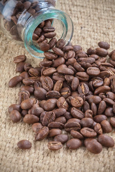 Coffee beans spilled out from glass little jar — Stock Photo, Image