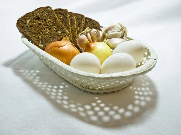 Cheese, eggs, bulb and garlic in a wum basket — Stock Photo, Image