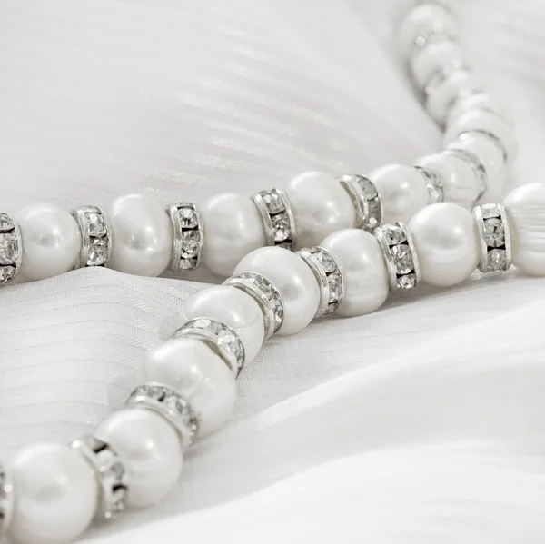 Colar de pérolas com anéis brilhantes de prata em um tecido de seda — Fotografia de Stock