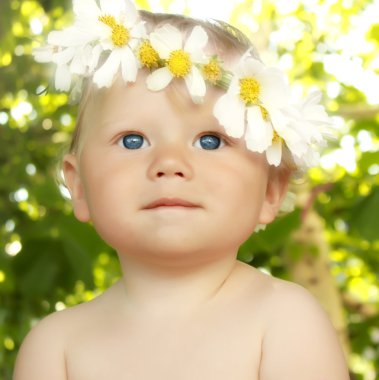 Smiling baby in a flower wreath in green summer background clipart