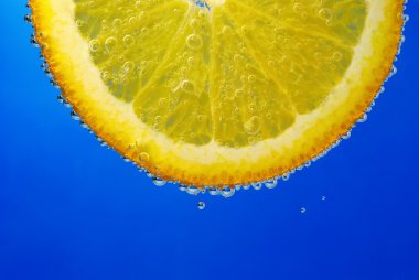 Part of the orange in the water with bubbles on a blue background clipart