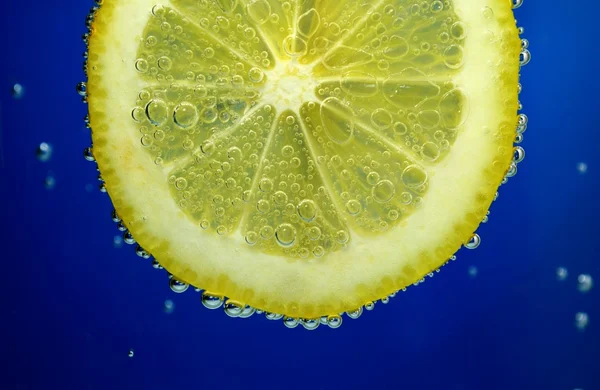 Parte de um limão na água com frascos em um fundo azul-escuro — Fotografia de Stock