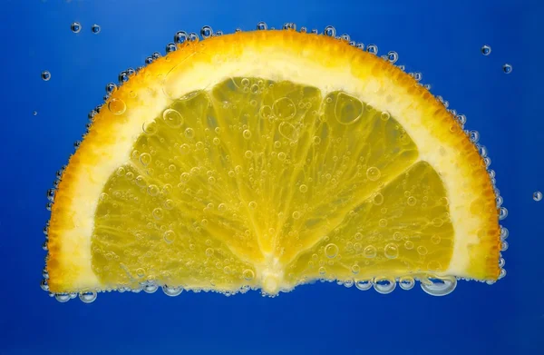 Parte da laranja na água com bolhas em um fundo azul — Fotografia de Stock