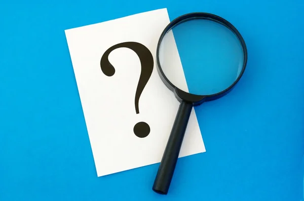 stock image A question mark on the paper and a magnifying glass
