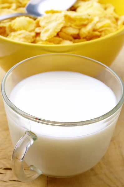 Молоко в стакане и кукурузные хлопья в желтой миске — стоковое фото