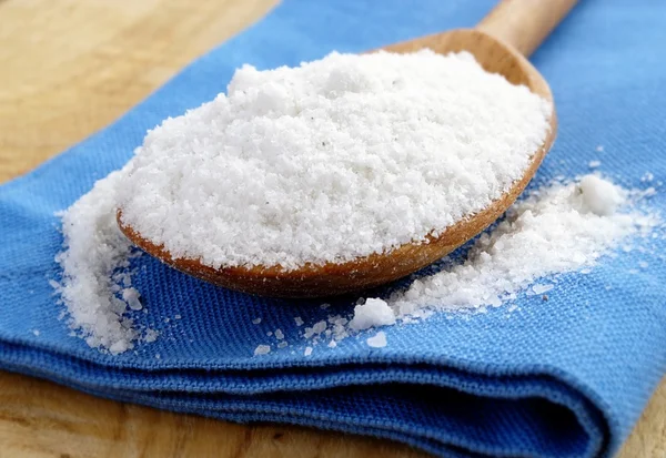 Salt in a brown wooden spoon and a blue cloth — Stock Photo, Image