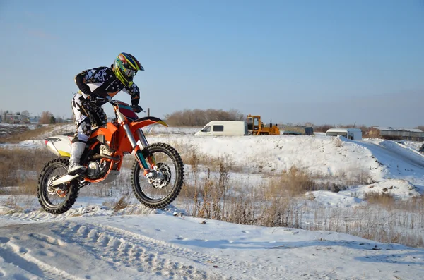 Motociclista en la bicicleta salta desde una colina en una altura nevada Fotos de stock libres de derechos