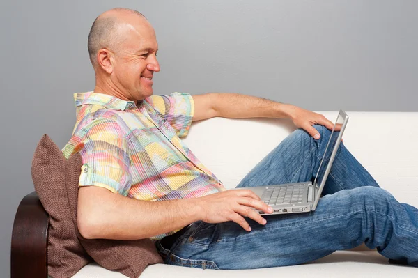 Senior man with notebook lying on the sofa at home — Stock Photo, Image