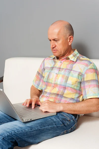 Senior man in spijkerbroek zitten met laptop thuis — Stockfoto