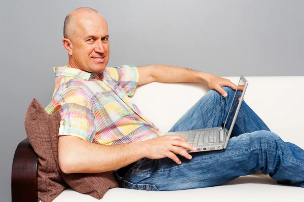 Oudere man met laptop op sofa — Stockfoto
