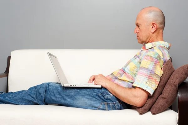 Homme sur le canapé blanc avec ordinateur portable — Photo