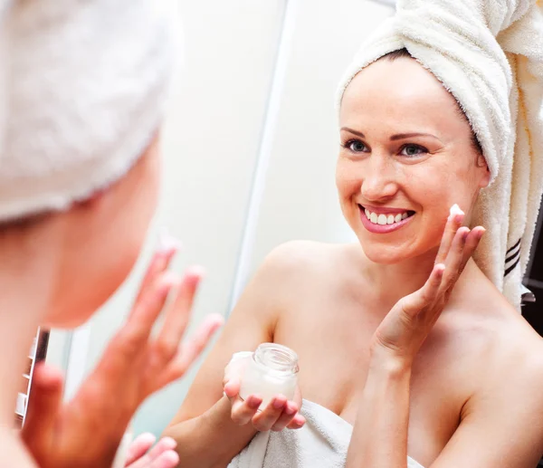Woman looking in mirror and applying cream — Stock Photo, Image