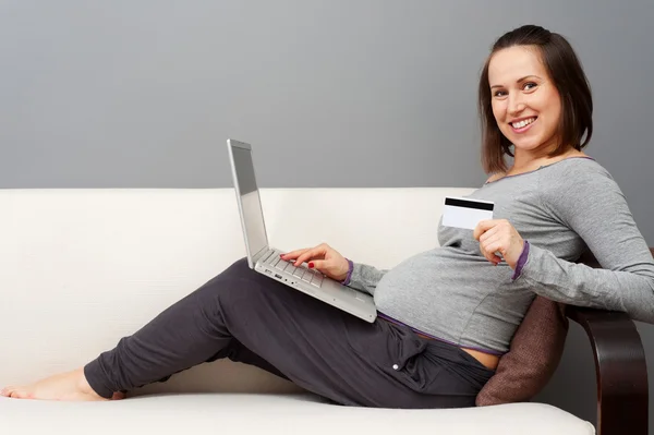 Pregnant woman holding laptop and showing credit card — ストック写真