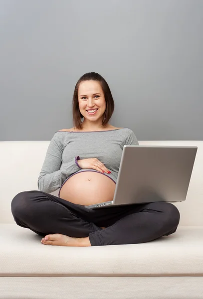 Беременная женщина отдыхает на диване с ноутбуком — стоковое фото