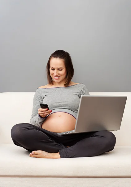 Mujer embarazada con teléfono celular y portátil — Foto de Stock