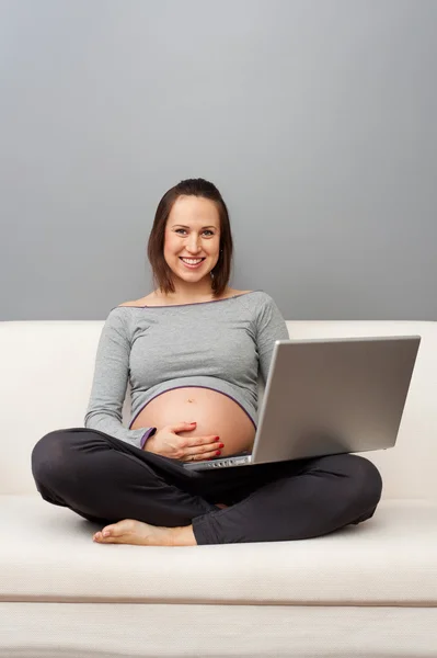 Έγκυος γυναίκα με φορητό υπολογιστή κάθεται στον καναπέ — Φωτογραφία Αρχείου