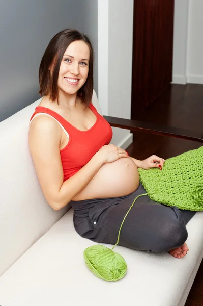Έγκυος γυναίκα κάθεται στον καναπέ και βελονάκι — Φωτογραφία Αρχείου
