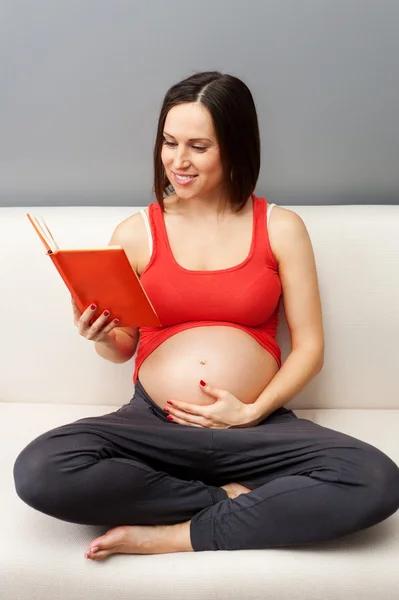 Těhotná žena sedí na pohovce s knihou — 图库照片