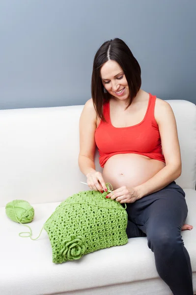 Беременная женщина вяжет крючок дома — стоковое фото