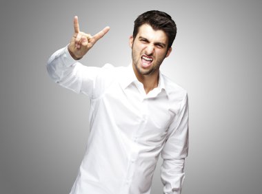 Portrait of young man doing rock symbol on grey background clipart