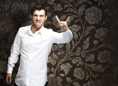 Portrait of young man doing rock symbol against a vintage wall clipart