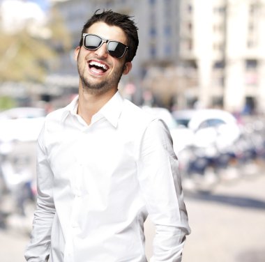 Portrait of young man with sunglasses laughing at city clipart