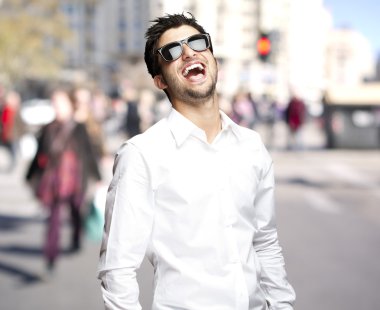 Portrait of young man with sunglasses laughing at city clipart