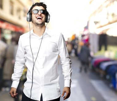 Portrait of young man laughing and listening to music at street clipart