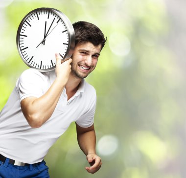 Portrait of a handsome young man carrying a clock against a natu clipart