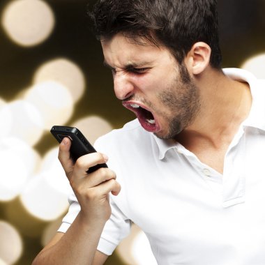 Portrait of angry young man shouting using mobile against a abst clipart