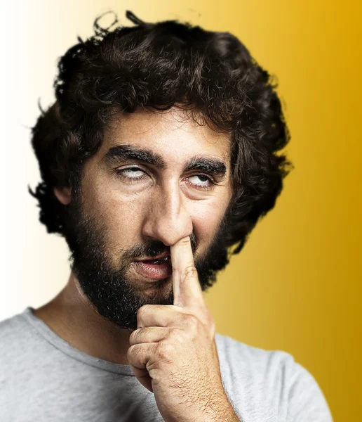 Young man with the finger in his nose over yellow background — Stock Photo, Image