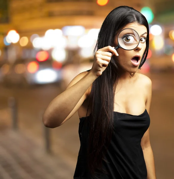 Jovem mulher surpreendida olhando através de uma lupa na cidade — Fotografia de Stock