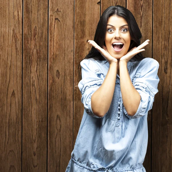 Portrait of young woman surprised against a wooden wall — Stock Photo, Image