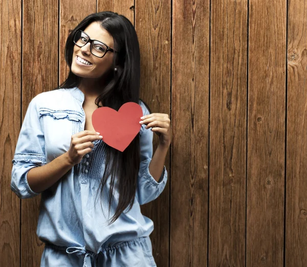 Portrait of young woman holding heart symbol against a wooden wall — Stock Photo, Image