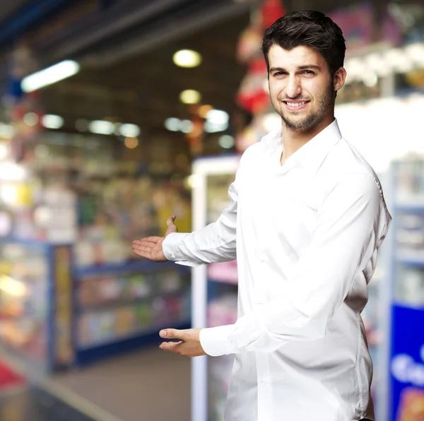 Porträtt av en stilig ung man inbjudande att komma in till butiken — Stockfoto
