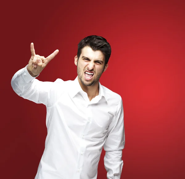 Портрет молодого человека, изображающего рок-символ на красном фоне — стоковое фото