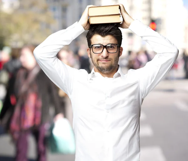 Porträtt av ung student håller böcker på huvudet på street — Stockfoto