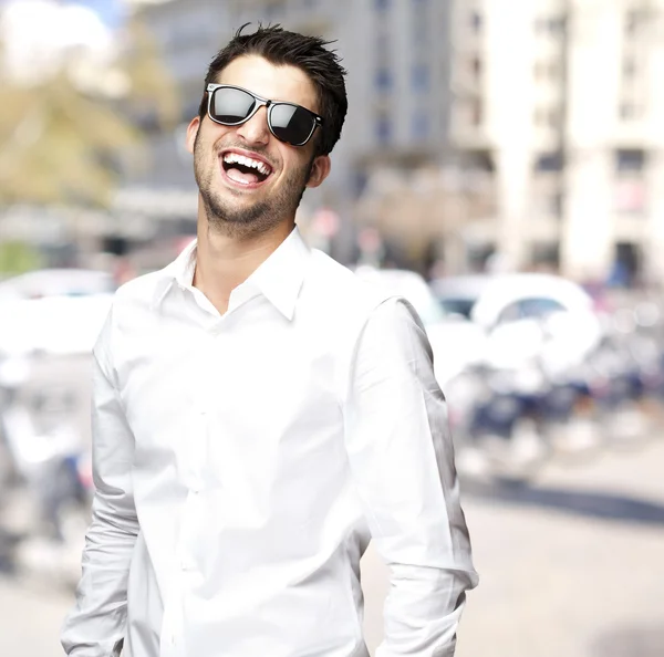 Portret van een jonge man met zonnebril lachen om stad — Stockfoto