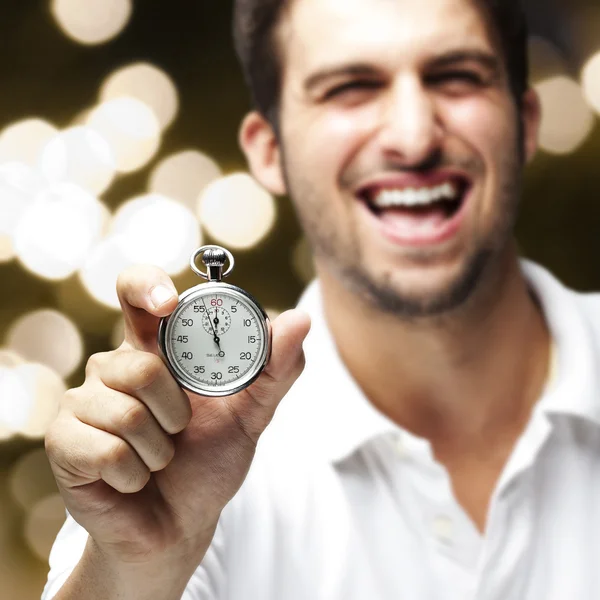 Retrato de un joven riendo y mostrando un cronómetro contra un —  Fotos de Stock