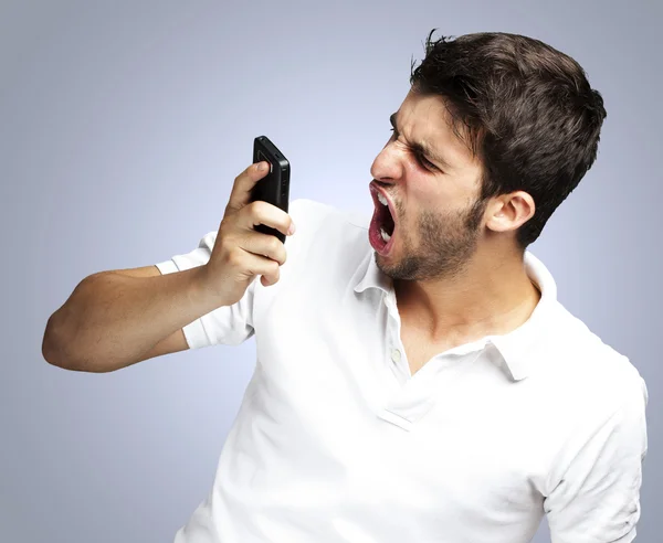 Kızgın genç adam bağırmaya kullanarak üzerinde mavi arka mobil portre — Stok fotoğraf