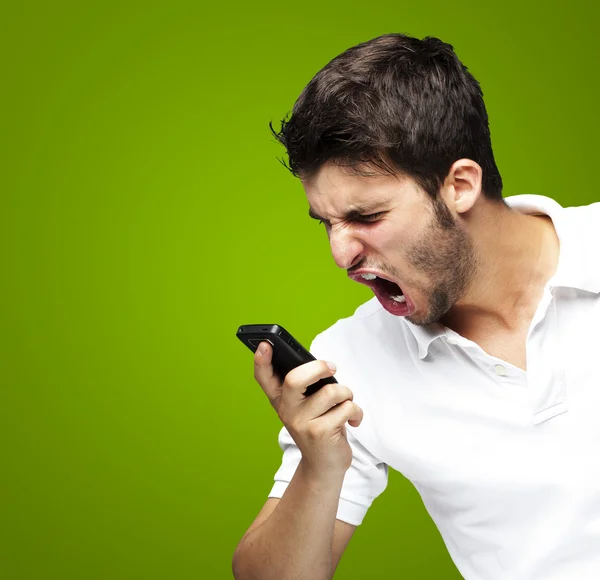 Портрет разгневанного молодого человека, кричащего на мобильном телефоне над зеленым пляжем — стоковое фото