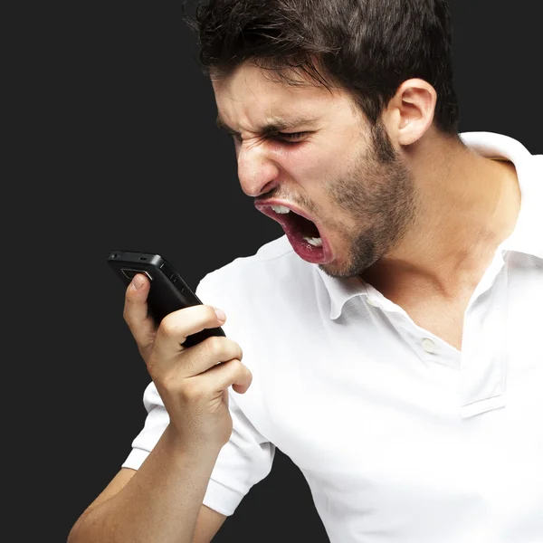 Retrato de um jovem bravo gritando usando celular sobre bac preto — Fotografia de Stock