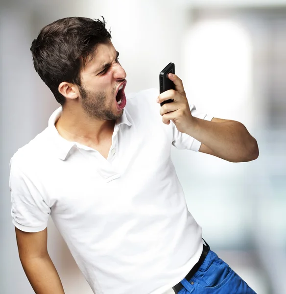 Portrait of angry young man shouting using mobile indoor — Stock Photo, Image
