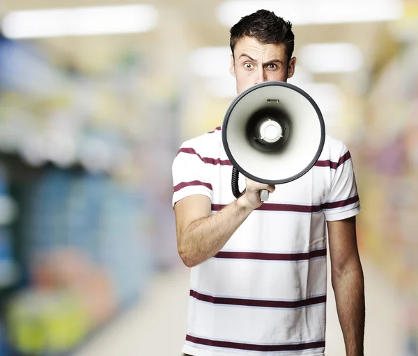 Портрет молодого человека, кричащего с мегафоном на рынке — стоковое фото