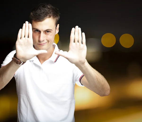 Portret młodego człowieka robi zdjęcie gest przeciwko streszczenie bac — Zdjęcie stockowe