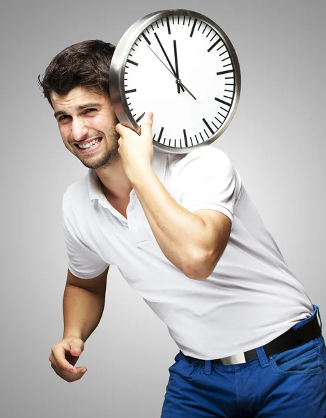 Portret van een knappe jongeman met een klok tegen een grijze Stockafbeelding